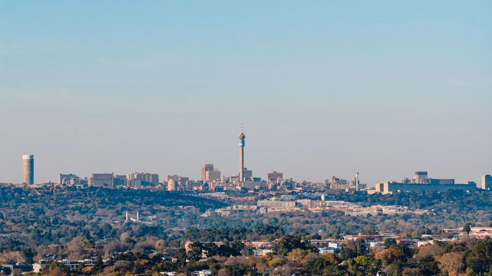 The Johannesburg skyline at dusk across the city's treed suburbs